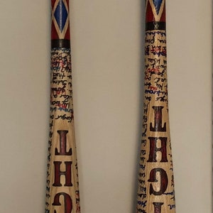 May include: Two wooden baseball bats with grey tape on the handle. The bats are painted with red and blue diamond patterns and have the words "GOOD NIGHT" written on them in red.