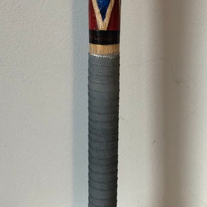 May include: A wooden baseball bat with a grey grip and a red, white and blue diamond pattern. The bat is painted with black and white writing.