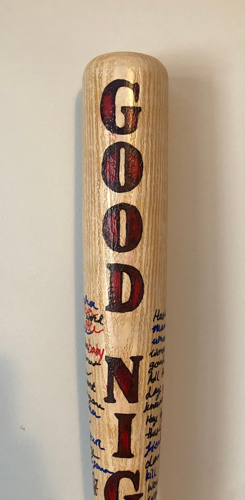 May include: A wooden baseball bat with the word "GOODNIGHT" painted in red and black letters. The bat is covered in blue and black writing.