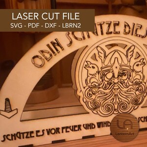 以下が含まれることがあります： 「ODIN SCHATZE DIE」と「SCHATZE ES VOR FEVER UND WIND」の文字が入ったレーザーカット木製ファイル。ひげを生やした人物とヘルメットと鳥の精巧な描写、そして「LASER CUT FILE SVG - PDF - DXF - LBRN2」の文字が含まれています。