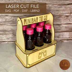 Könnte beinhalten: Ein lasergeschnittener Minibar-Träger aus Holz mit dem Text "MINIBAR TO GO". Er fasst sechs kleine Flaschen mit rosa Kappen. Der Träger hat einen Griff und ein dekoratives Design von zwei Gläsern. Der Text "LASER CUT FILE" steht oben.