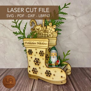 Könnte beinhalten: Weihnachtliche Stiefeldekoration aus Holz, lasergeschnitten, mit Stern- und Schneeflockenmotiven. Der Stiefel ist mit kleinen Holzspielzeugen und Grünzeug gefüllt. Der Text "Fröhlichen Nikolaus" ist zu sehen. Der Text "LASER CUT FILE" und Dateityp-Abkürzungen sind ebenfalls vorhanden.