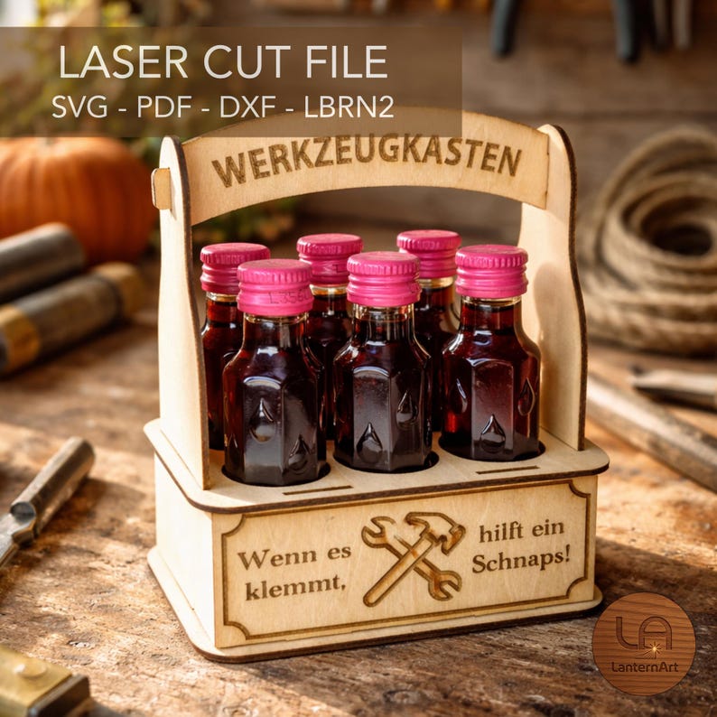May include: A wooden laser-cut file of a toolbox design, holding six small bottles with pink caps. The text "WERKZEUGKASTEN" is arched across the top. The bottom of the box has the text "Wenn es klemmt, hilft ein Schnaps!"