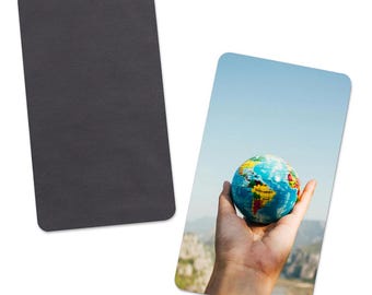 Op de afbeelding: Twee rechthoekige magneten. Eén is effen zwart. De andere toont een hand die een kleine wereldbol vasthoudt tegen een achtergrond van een blauwe lucht en bergen. De wereldbol is blauw, geel en groen.