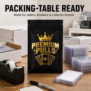 May include: A black resealable pouch featuring a gold crown icon and the text PREMIUM PULLS. The pouch is centered among shipping supplies including a tape dispenser, white cardboard boxes, and clear plastic card cases on a wooden surface.