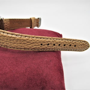 May include: A brown leather watch band with white stitching and a silver buckle.