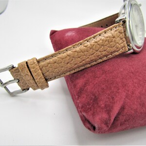 May include: A silver watch with a brown leather band. The watch is on a red velvet cushion.