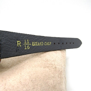K&ouml;nnte beinhalten: Ein schwarzes Lederarmband mit goldenen Akzenten und dem aufgedruckten Text "R 11/16 LIZARD CALF".