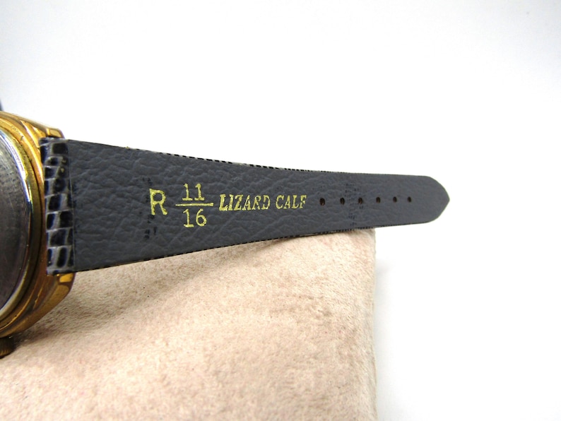K&ouml;nnte beinhalten: Ein schwarzes Lederarmband mit goldenen Akzenten und dem aufgedruckten Text "R 11/16 LIZARD CALF".