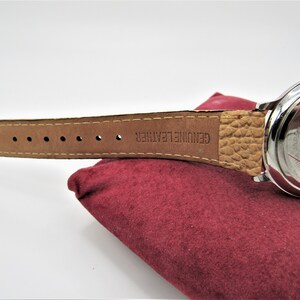 May include: A silver wristwatch with a brown leather band. The band is embossed with the words "GENUINE LEATHER". The back of the watch has the words "MADE IN CHINA" and "LP DESIGN" printed on it.