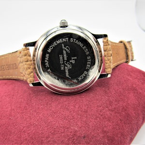 May include: Back of a silver wristwatch with a brown leather band. The watch face says "LP Lucien Piccard 2802-TN Made in China Japan Movement Stainless Steel Back".