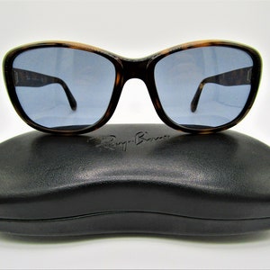 May include: Tortoise shell Ray-Ban sunglasses with blue lenses and a black leather case. The case has the Ray-Ban logo embossed on the front.