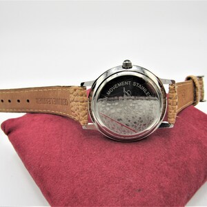 May include: Back view of a silver wristwatch with a brown leather band. The watch face has the text "Swiss Movement Stainless Steel" engraved on it.