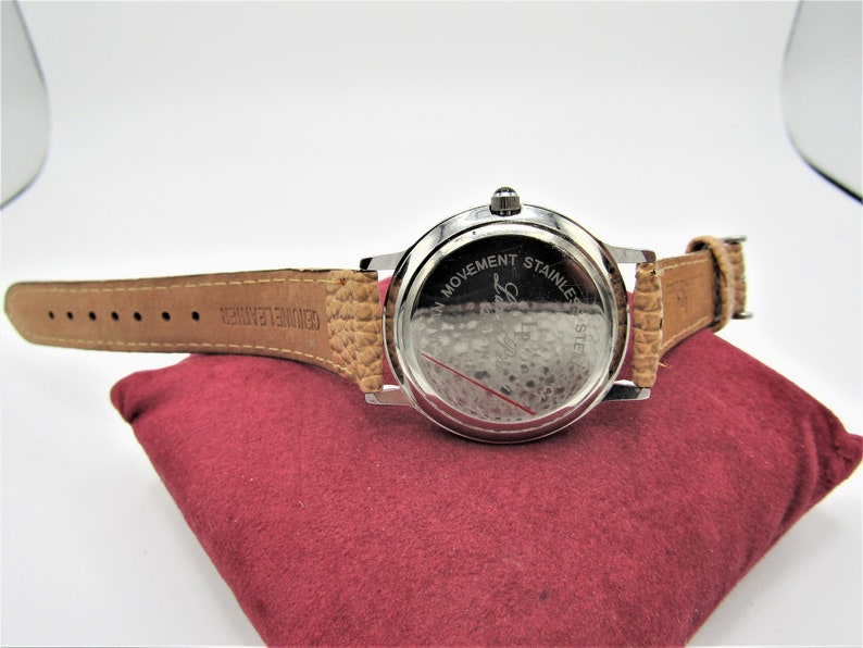 May include: Back view of a silver wristwatch with a brown leather band. The watch face has the text "Swiss Movement Stainless Steel" engraved on it.