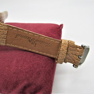 May include: A brown leather watch strap with the text "Lauren, New York" embossed on it.