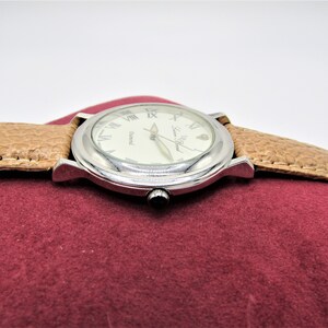 May include: A silver wristwatch with a white face and Roman numeral hour markers. The watch has a brown leather band and the words "Swiss Made" are printed on the face.
