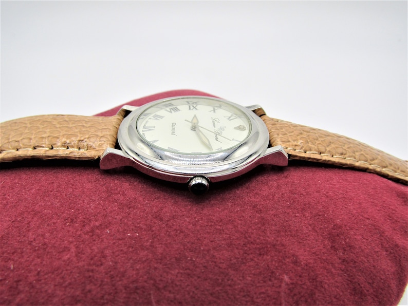 May include: A silver wristwatch with a white face and Roman numeral hour markers. The watch has a brown leather band and the words "Swiss Made" are printed on the face.