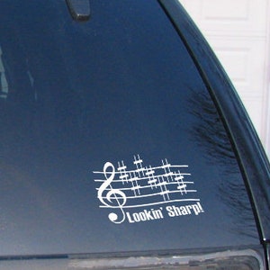 Puede incluir: Un coche negro con una calcomanía de vinilo blanco en la ventana trasera. La calcomanía presenta una clave de sol y notas musicales con el texto "Lookin' Sharp!"
