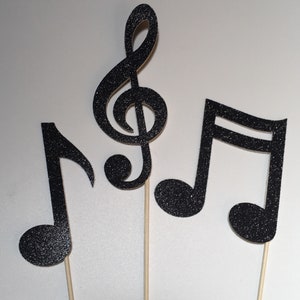 May include: Three black glitter musical note decorations on wooden sticks. The set includes a treble clef, a quarter note, and an eighth note. These musical decorations are perfect for a music-themed party or event.
