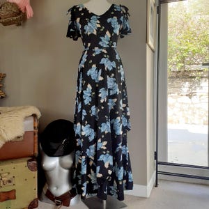 May include: A long black maxi dress with a blue and white floral print. The dress has a V-neckline, short sleeves, and a tie belt at the waist.