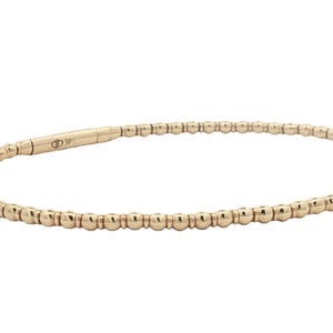 May include: A gold-colored beaded bracelet. The bracelet is made of small, round beads strung together to form a flexible band. The clasp is a simple, streamlined design. The bracelet is shown against a white background.