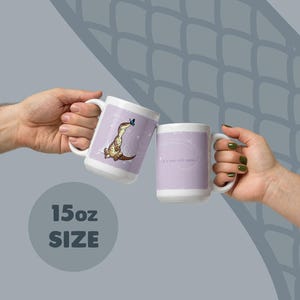 May include: Two white 15oz ceramic mugs featuring a light purple background. One mug displays a brown lizard with a blue butterfly on its nose. The other mug features the text 'Life is better with reptiles' in a white script font on a purple field.