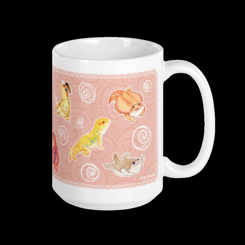 May include: White ceramic mug with a pink background and a pattern of swirling lines. The mug features illustrations of bearded dragons in various poses. The text "Fatty Pancakes" is printed on the bottom right corner of the mug.