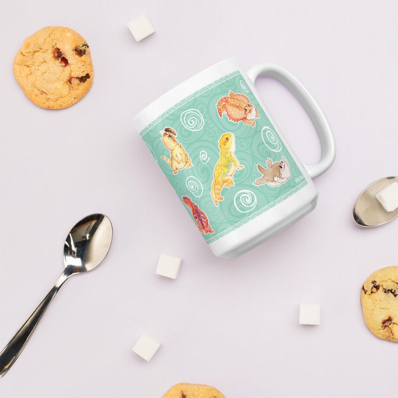 May include: White ceramic mug with a teal background and a pattern of swirling lines. The mug features a repeating design of cartoon bearded dragons in various poses.