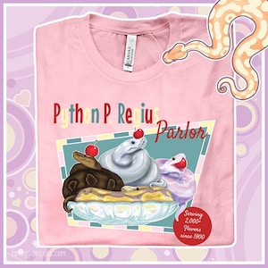 Op de afbeelding: Roze T-shirt met een retro-stijl illustratie van drie ball pythons in een bananensplit sundae. De tekst luidt "Python P. Regius Parlor" en "Serving 2,000+ Flavors since 1900".