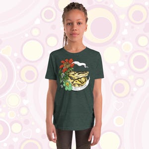 Może przedstawiać: Zielony t-shirt z nadrukiem przedstawiającym węża boa dusiciela zwiniętego z kwiatami i tekstem "Ball Python".
