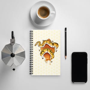 May include: A spiral-bound notebook featuring a yellow honeycomb pattern background with a central illustration of a yellow and black patterned snake coiled around a piece of dripping honeycomb, surrounded by several small flying bees.