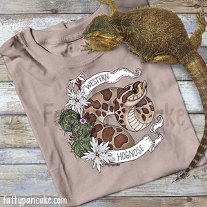 May include: A beige t-shirt with a graphic of a Western Hognose snake curled up with cactus and flowers. The text "Western Hognose" and "Fatty Pancake" are on the banner.