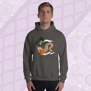Op de afbeelding: Donkergrijze hoodie met een kleurrijke afbeelding. De afbeelding toont een boom, oranje bloemen en een slangachtig wezen met de tekst "Rosy Boa" op een spandoek. De hoodie heeft een voorzak en een capuchon.