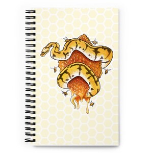 A spiral-bound notebook with a pale yellow honeycomb pattern cover, featuring an illustration of a yellow and black snake wrapped around a honeycomb structure. The notebook is displayed on a bright white background.