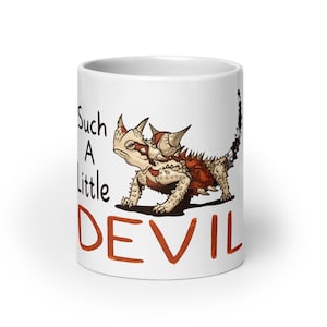 May include: A white ceramic mug featuring a detailed illustration of a horned lizard with spikes and a reddish-brown back. The text "Such A Little DEVIL" is printed in black and orange lettering on the side of the mug, positioned next to the lizard.