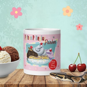 May include: A white ceramic mug featuring a graphic of three snakes in an ice cream sundae dish. The text reads Python P. Regius Parlor and Serving 2,000+ Flavors since 1900. The design includes red cherries, starburst accents, and a pink background.