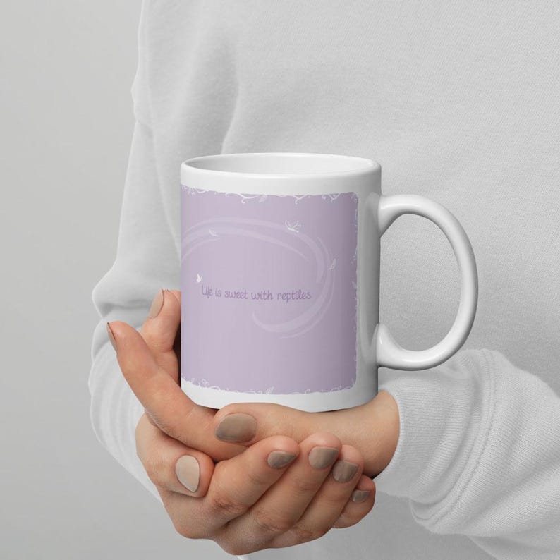 May include: A white ceramic mug featuring a light purple rectangular graphic on the side. The graphic contains the text "Life is sweet with reptiles" in a simple font, surrounded by faint white swirling lines and small butterfly silhouettes.