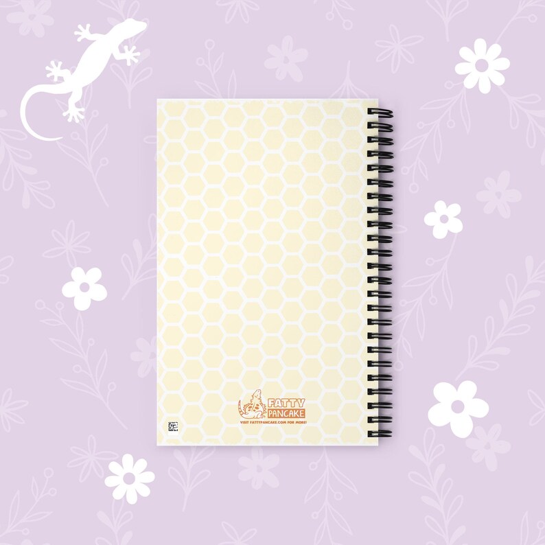 A spiral-bound notebook with a pale yellow and white honeycomb pattern cover, featuring the 'Fatty Pancake' logo at the bottom, displayed on a light purple floral background.