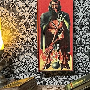 May include: A vintage illustration of a red devil with horns, a forked tail, and a long, pointed beard. The devil is holding a pitchfork and a chain with a ball and chain attached to his ankle. The illustration is on a red background with flames at the bottom.