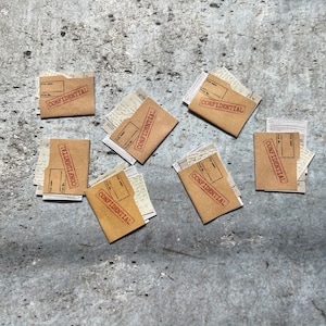 May include: A flat lay of six brown envelopes with the word "CONFIDENTIAL" stamped in red on each. The envelopes are scattered on a gray concrete surface.