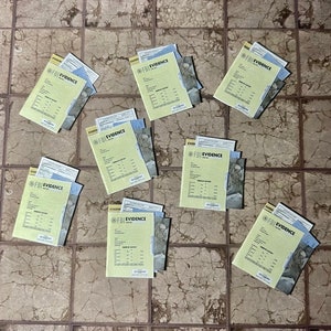 May include: Nine yellow and white FBI evidence bags laid out on a tiled floor. The bags are labeled "FBI EVIDENCE" in black text.