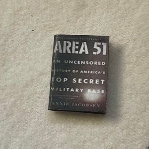 May include: A black book with the title "Area 51: An Uncensored History of America's Top Secret Military Base" by Annie Jacobsen.