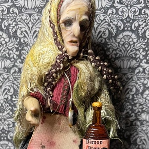 May include: A doll dressed as an old woman with a brown and white shawl, holding a small bottle labeled "Demon Brew".