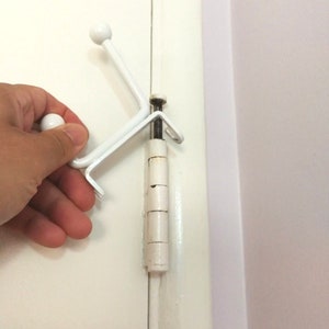 May include: White plastic door hook with a round knob on the end. The hook is attached to a white door hinge.