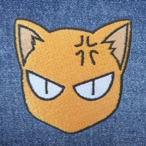 May include: Orange embroidered patch of a cat with angry eyes and the Japanese characters "J.L. 77" on its forehead.