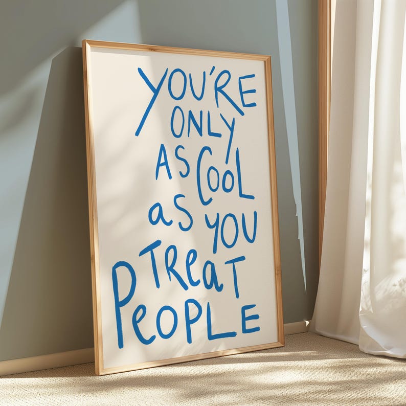 May include: A framed print with the text "You're only as cool as you treat people" written in blue cursive on a white background.