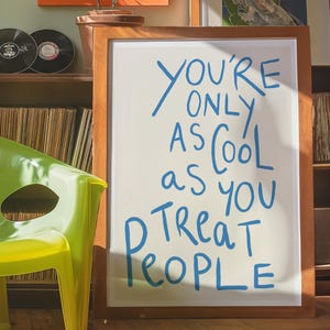 May include: A wooden framed sign with a white background and blue lettering that reads "You're only as cool as you treat people".