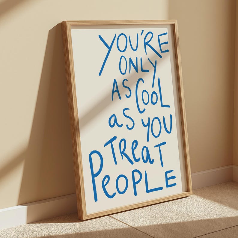 May include: A framed print with a white background and blue text that reads "You're only as cool as you treat people".