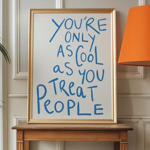 May include: A gold framed poster with a white background and blue text that reads "You're only as cool as you treat people".