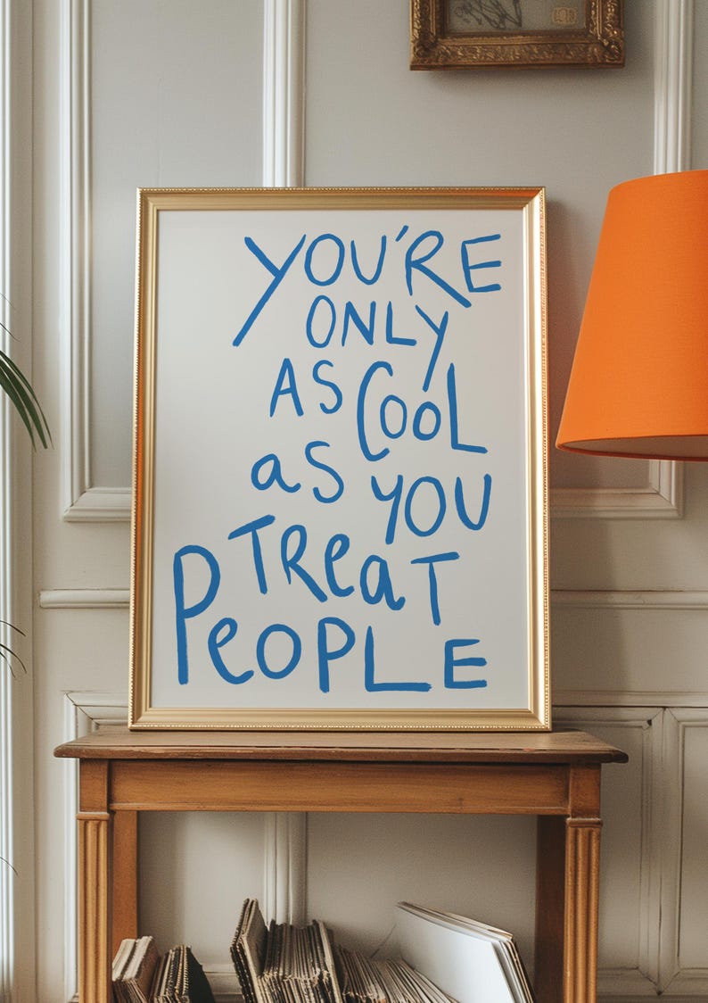 May include: A gold framed poster with a white background and blue text that reads "You're only as cool as you treat people".